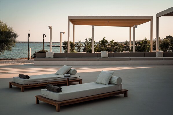 A modern outdoor lounge area with seating and a pergola overlooking a body of water.
