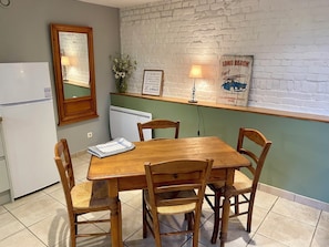Un coin repas avec une table et des chaises en bois, un réfrigérateur blanc, un miroir, une lampe fixée au mur et un panneau décoratif encadré.