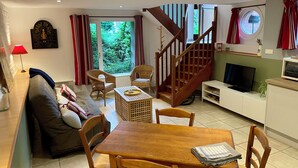 Un salon comprenant un canapé, une table à manger en bois, des chaises, un téléviseur, un escalier et une fenêtre avec des rideaux.