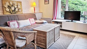 Une pièce comprenant un canapé, un téléviseur, une lampe, un tableau et une fenêtre avec des rideaux.