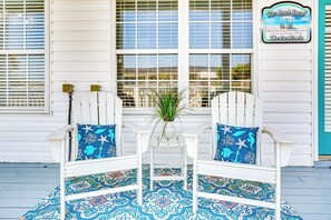 A porch with two white Adirondack chairs, a small table, and a potted plant. - Pelican Manor D (North Myrtle Beach)