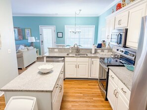 A kitchen with white cabinets, a granite countertop, a stainless steel refrigerator, and a built-in oven. - Pelican Manor D (North Myrtle Beach)