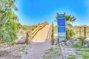 Ein hölzerner Steg führt zu einem Strandbereich, wobei ein Wegweiser Informationen bietet.