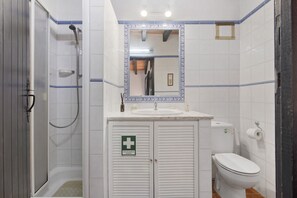 Casa de banho com chuveiro, lavatório, sanita e espelho com moldura decorativa.