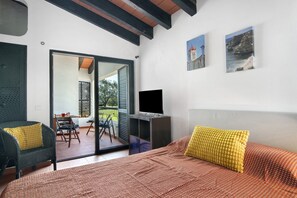 Ein Schlafzimmer mit einem Bett, einem Fernseher, einem Sessel, einem Tisch und einer Schiebetür zu einem Außenbereich.