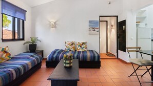 A compact room with a bed, a small table with a plant, a sofa, and a chair.