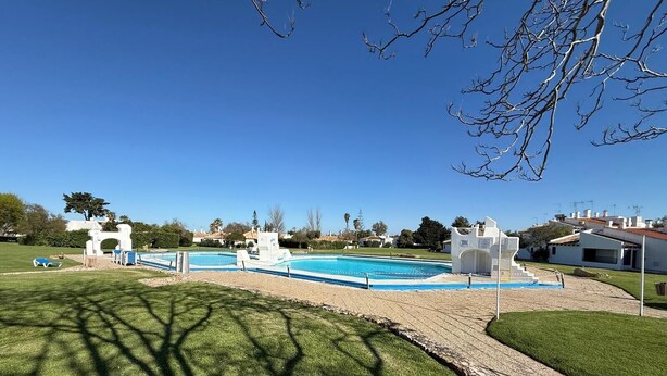 A swimming pool with a white structure, a grassy area, and a clear blue sky.