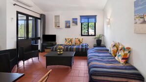 A room with a sofa, a chair, a table, and a TV.