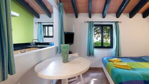 Una habitación con cama, mesa, televisor y ventana con cortinas.