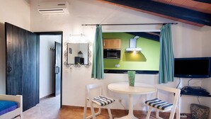 Una habitación con cama, una mesa de comedor con sillas, televisión, zona de cocina y espejo.
