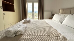 Ein Hotelzimmer mit Bett, Kleiderschrank, einem Fenster mit Vorhängen und Blick ins Freie.