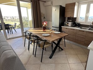 A modern kitchen with a dining table, chairs, a refrigerator, and a view of the outdoors. - Altamira II | 10 Guests | Veranda & Sea Views | Zakynthos (QV23+J4H, Zakinthos, Greece)