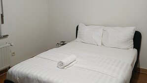 Ein Einzelbett mit weißen Bettwäsche, einem schwarzen Kopfteil und einem Holzboden.