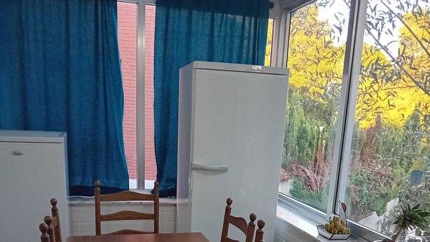 Ein Essbereich mit Holztisch und Stühlen, einem weißen Kühlschrank und einem Fenster mit Vorhängen.