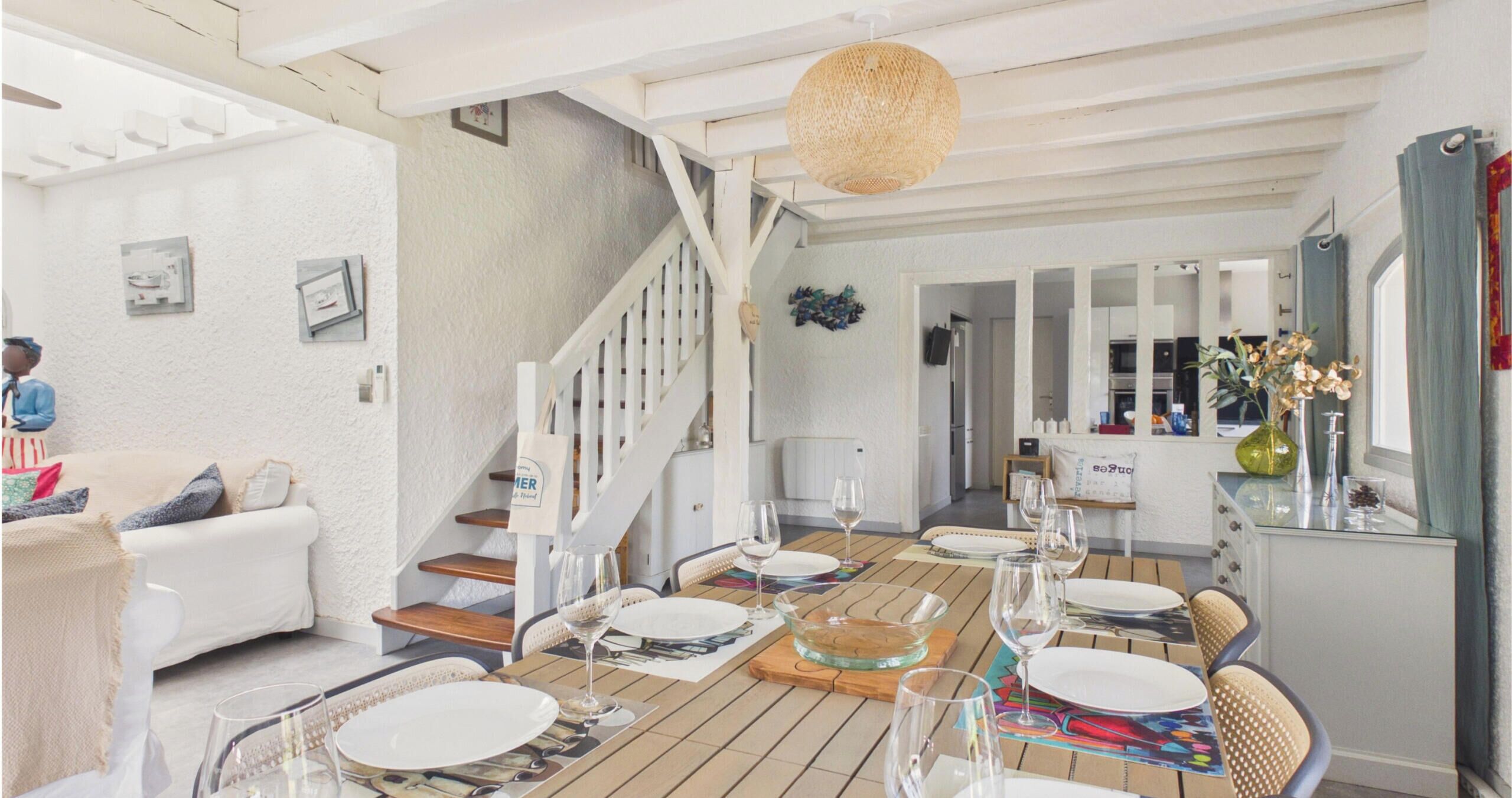 Ein Essbereich mit einem Holztisch, gedeckt für eine Mahlzeit, eine Treppe und eine Küche im Hintergrund.