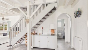 Un escalier menant à une salle de bain dont un mur est recouvert de carreaux, qui comprend également un meuble avec des tiroirs et un ventilateur de plafond.