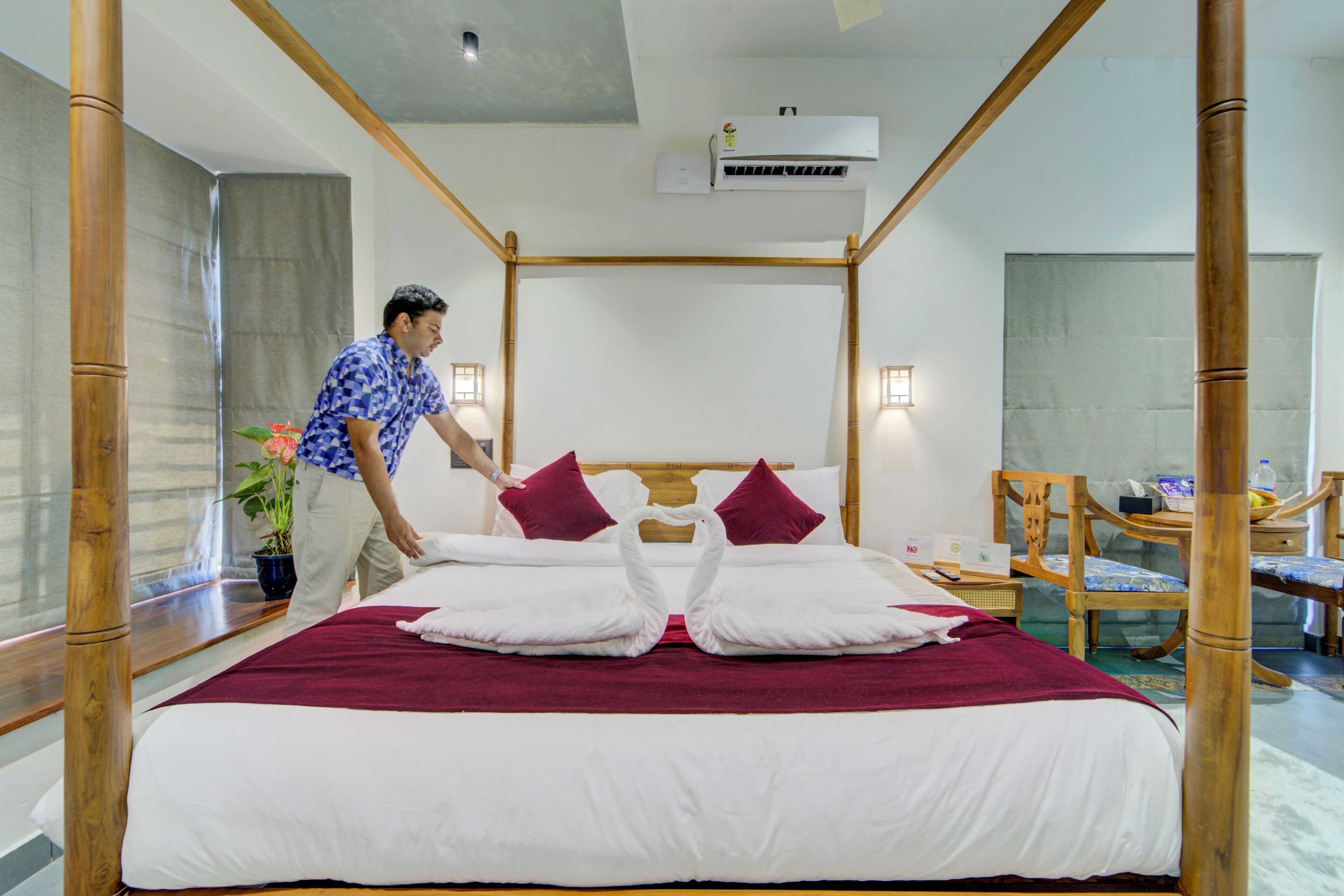 A hotel room with a bed, a wooden headboard, a potted plant, a desk, and a chair.