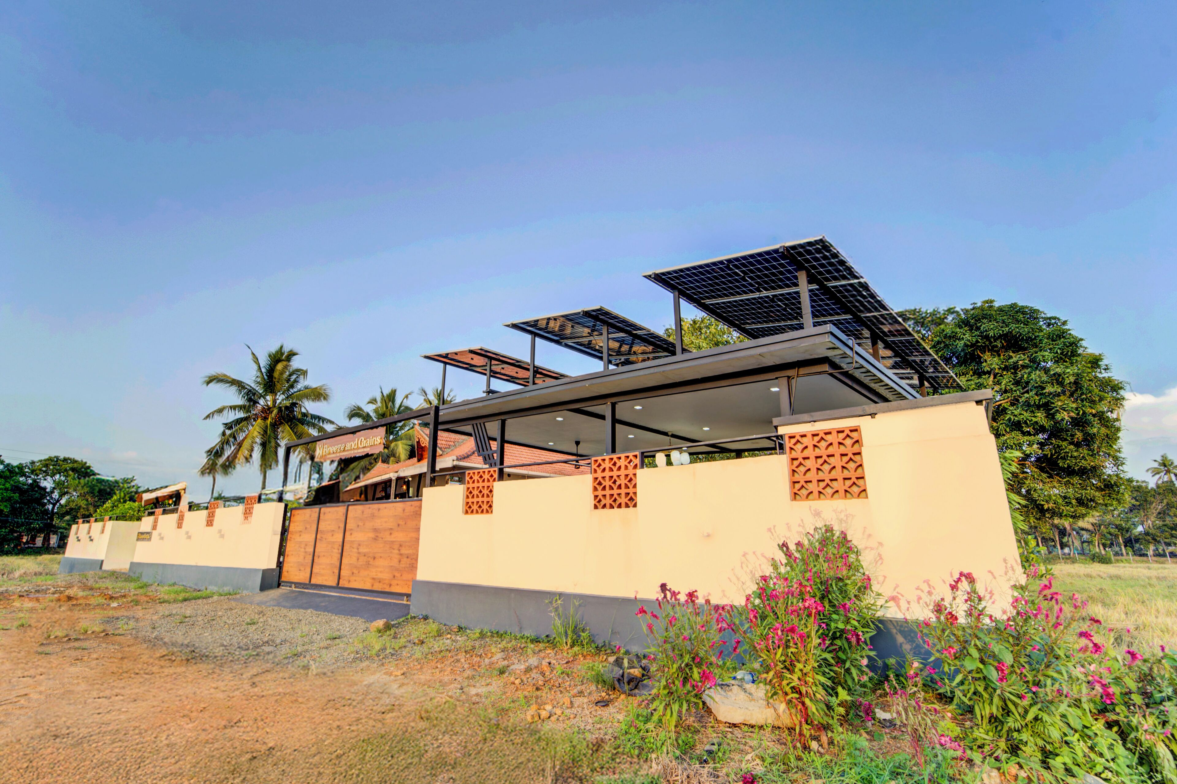 Un edificio moderno con paneles solares, una zona exterior cubierta y vistas a palmeras.