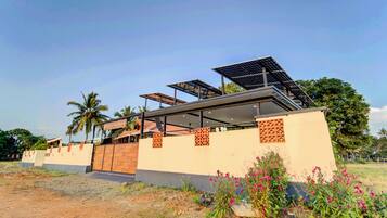 Un edificio moderno con paneles solares, una zona exterior cubierta y vistas a palmeras.