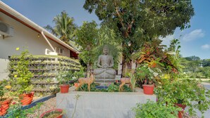 A statue of a seated figure surrounded by potted plants and a small fountain. - ELIVAAS Breeze & Grains 3BHK with Patio (Kuttanad Taluk)