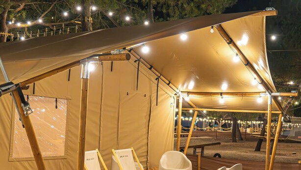 A tented outdoor area with wooden flooring, two white lounge chairs, and string lights. - Orla Ilha de Tavira Eco-Glamping (Tavira)