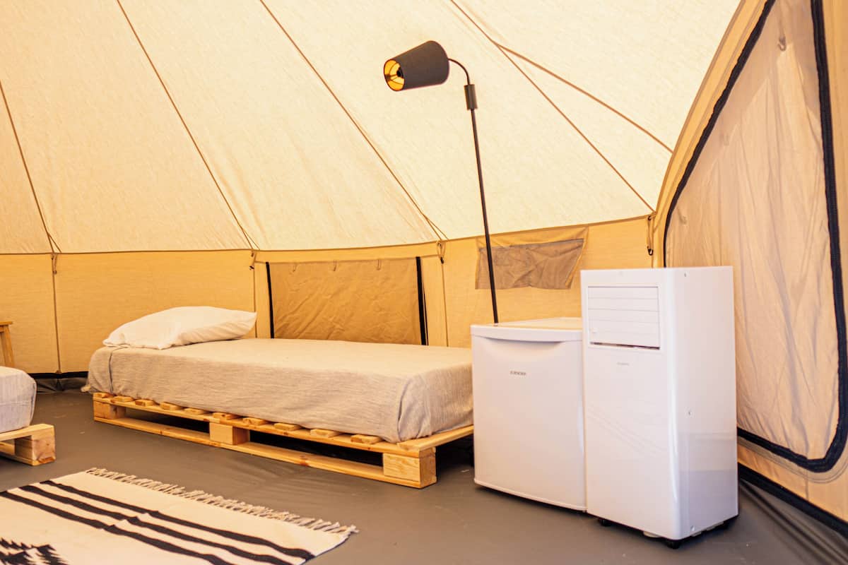 Ein Zelt mit Bett, einem kleinen Tisch, einer Lampe und einem Kühlschrank.