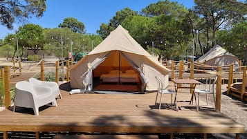 A tented accommodation with a wooden deck, a bed, and a seating area.