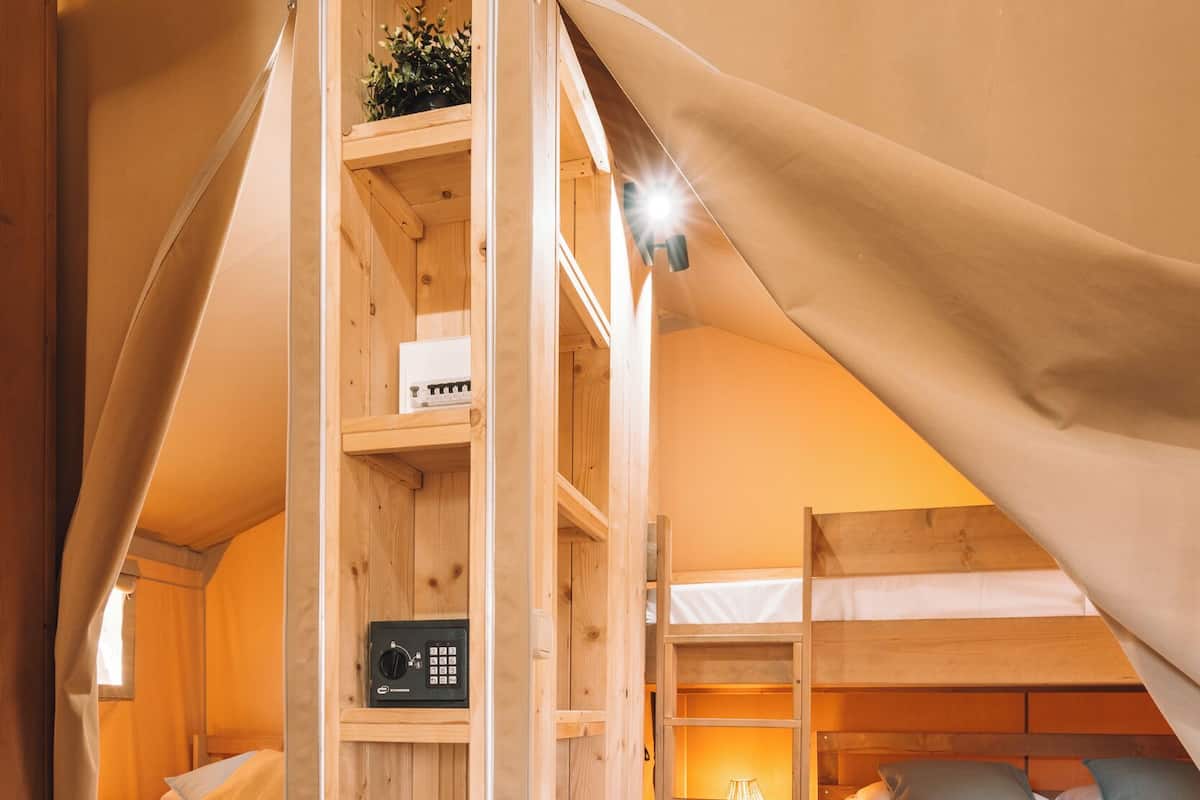 Ein gemütliches Zelt-ähnliches Zimmer mit zwei Etagenbetten, Holzregalen, einem kleinen Tisch und einer Lampe.