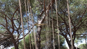 A rope bridge over a sandy area with trees and a small building in the background. - Orla Ilha de Tavira Eco-Glamping (Tavira)