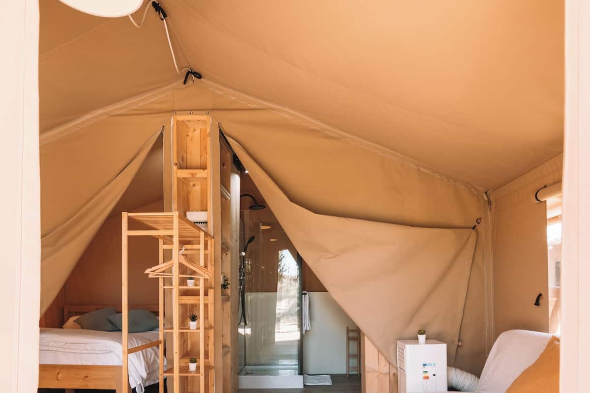Eine Zelthütte mit Etagenbett, einer Holzleiter, einem kleinen Tisch und einer Couch.