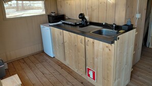 A compact kitchen with wooden cabinets, a sink, a small refrigerator, and a window. - Orla Ilha de Tavira Eco-Glamping (Tavira)