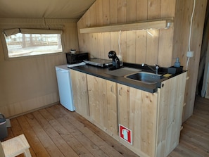 Una cocina compacta con armarios de madera, un lavamanos, un refrigerador pequeño y una ventana.