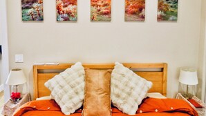 A bedroom with a wooden headboard, two pillows, a bed with an orange cover, and a wall with five landscape paintings.