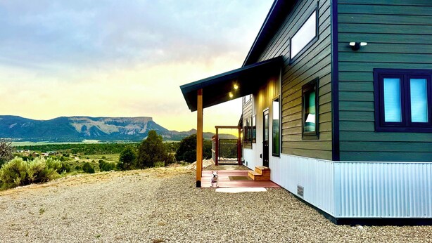 A modern house with a covered porch, a gravel driveway, and a mountainous landscape in the background.