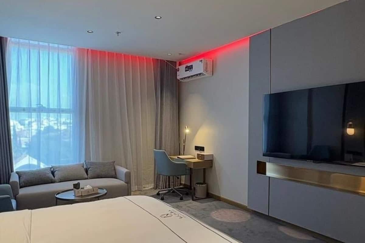 Une chambre d’hôtel moderne équipée d’un lit, d’un bureau, d’une chaise, d’une télévision et d’une grande fenêtre avec des rideaux.