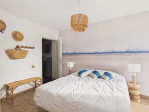 A bedroom with a bed, a bench, a hanging basket, and a painting on the wall. - 500 m from the beach – House for 6 with garden (Fouesnant)