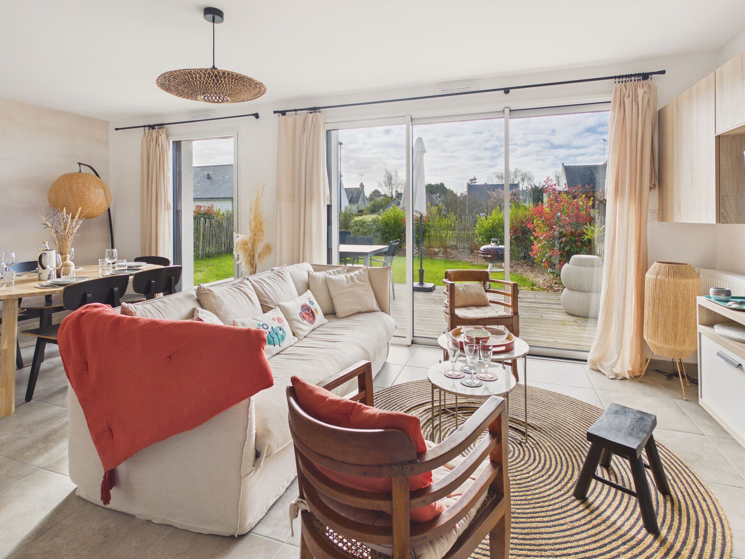 A modern living room with a sofa, chairs, a dining table, and a view through large glass doors to a garden.