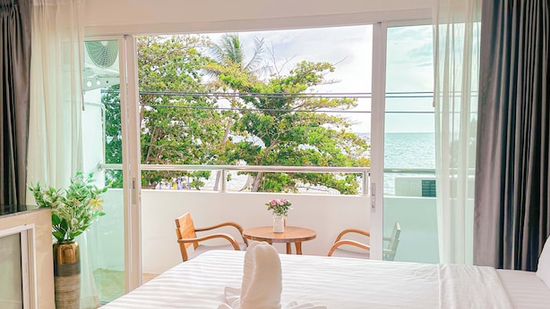 Une chambre d’hôtel avec un lit, un balcon doté d’une table et de chaises, et une vue sur la mer et les arbres.