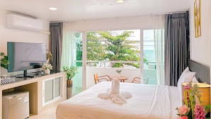 Une chambre d’hôtel comprenant un lit, un bureau avec une télévision, un mini-réfrigérateur, un balcon avec vue sur la mer et un coin repas.