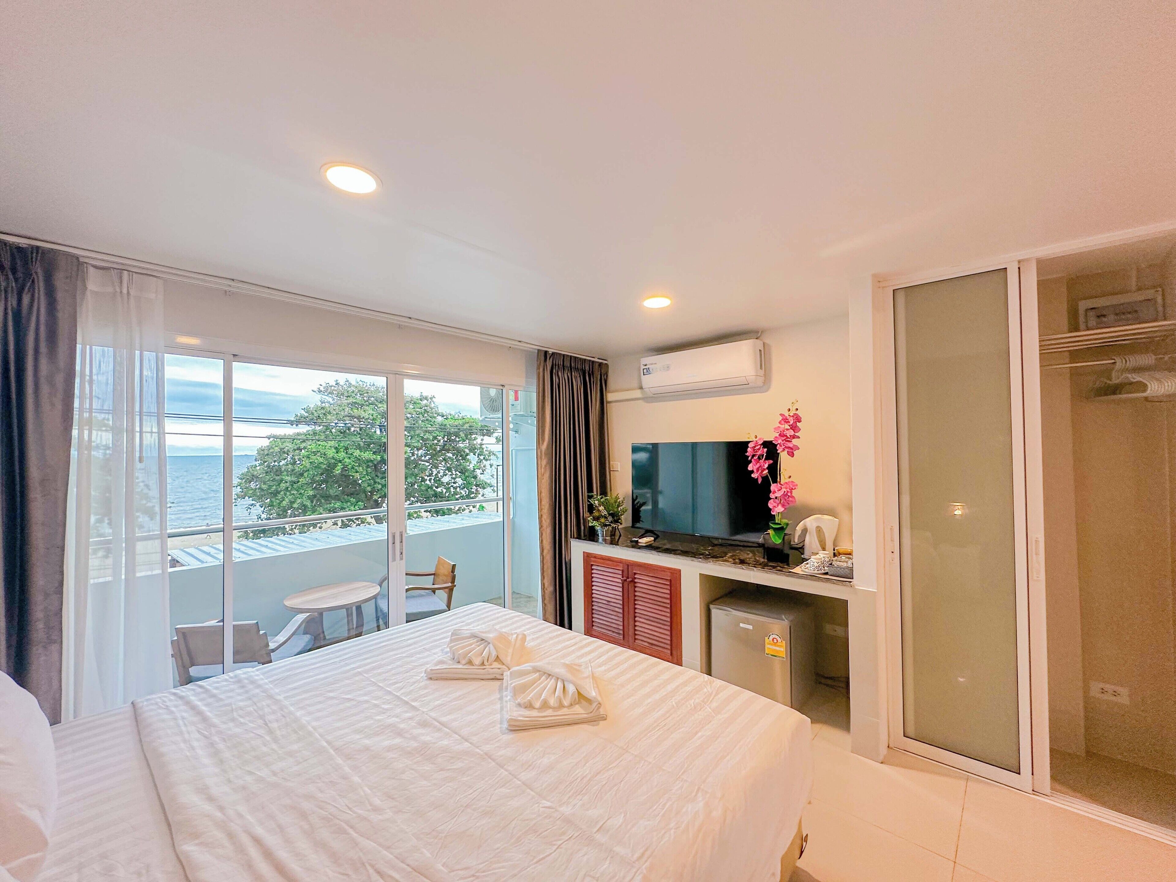 Habitación de hotel con cama, televisión, mini refrigerador, ducha y balcón con vista al mar.