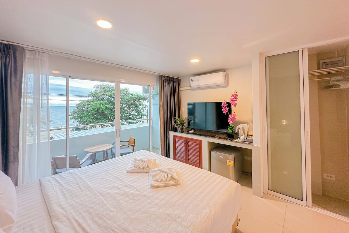 Ein Hotelzimmer mit Bett, Fernseher, Minikühlschrank, Dusche und einem Balkon mit Meerblick.