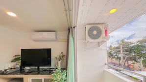Une chambre équipée d’une télévision, d’un appareil de climatisation, d’un petit réfrigérateur, d’une plante en pot et offrant une vue sur l’extérieur.