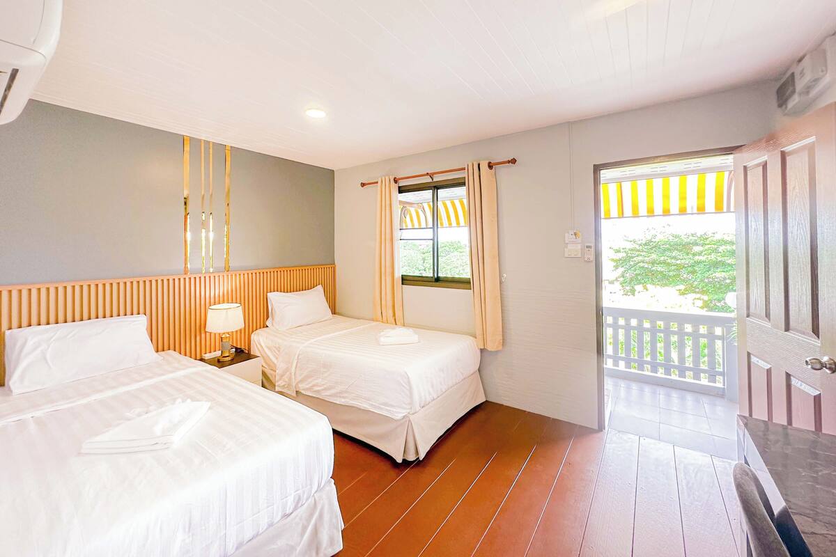 Habitación de hotel con dos camas, piso de madera, ventana con cortinas y puerta que da a un área exterior.