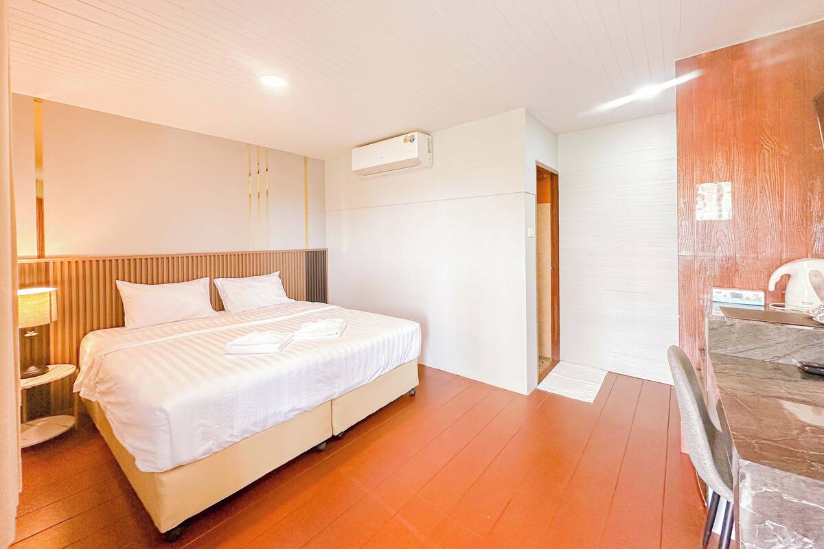 Habitación de hotel con cama, mesita de noche y baño con ducha y espejo.