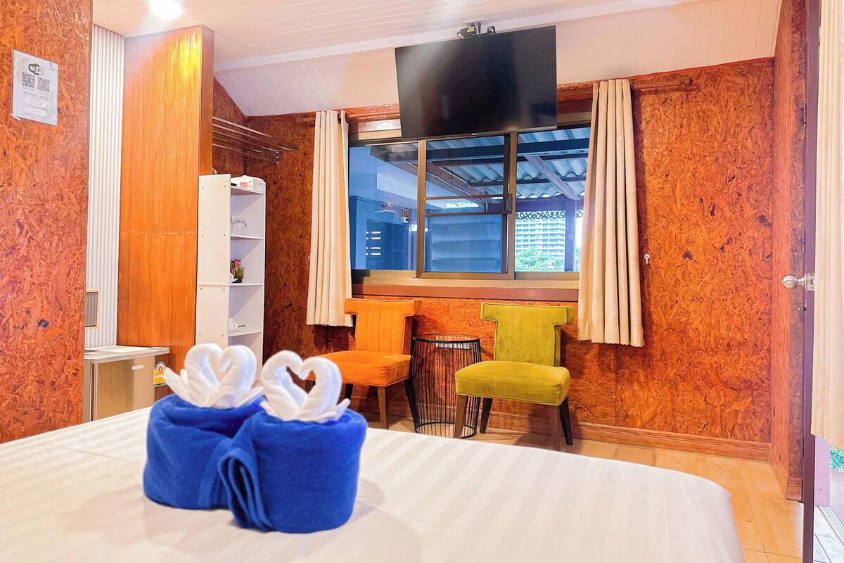 Una habitación de hotel con cama, televisión, ventana con cortinas, una mesita pequeña y una silla.