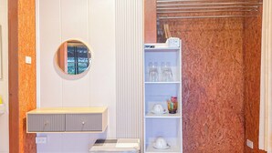 Ein kleines Zimmer mit Küchenzeile, einem runden Spiegel, einem Regal mit Geschirr und einer Sitzbank.