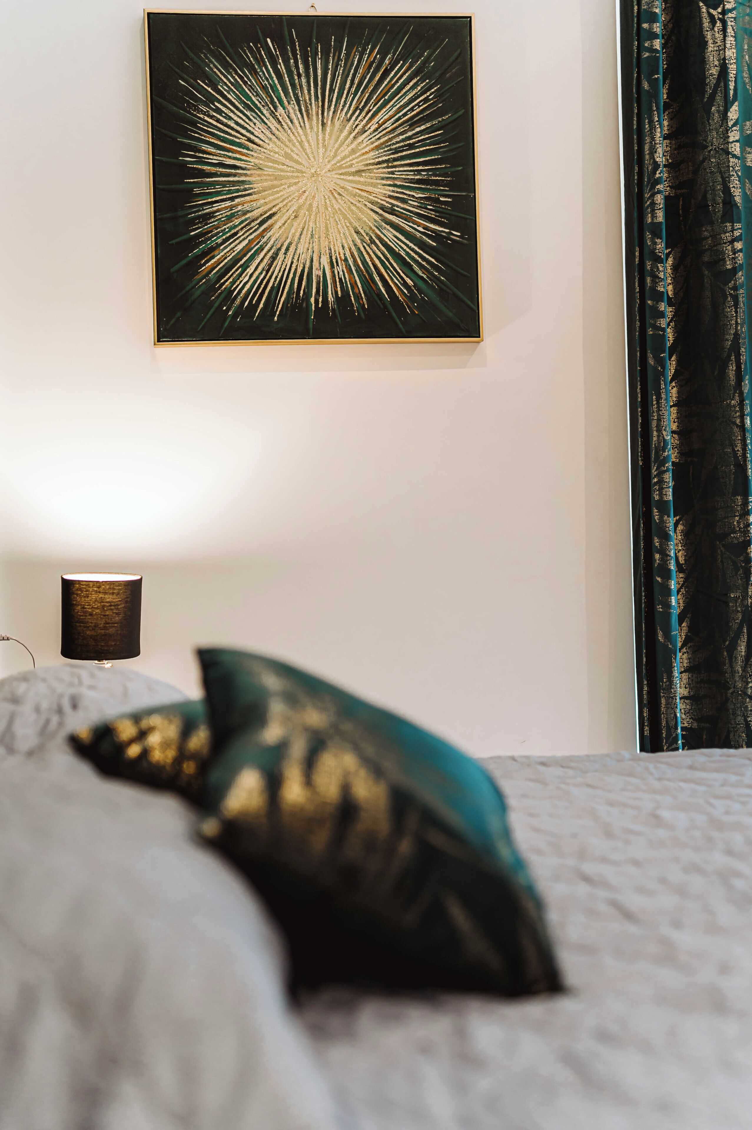 Una cama con un almohadón, un cuadro en la pared y una lámpara.