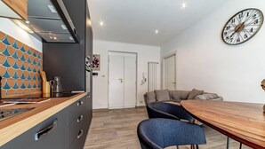 Une cuisine moderne avec un plan de travail en bois, un coin repas avec une table en bois et des chaises bleues, et une horloge murale.