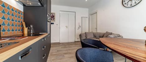 Eine moderne Küche mit Holzarbeitsplatte, ein Essbereich mit Holztisch und blauen Stühlen sowie eine Wanduhr.