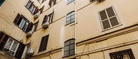 Ein mehrgeschossiges Gebäude mit einem zentralen Eingang, zahlreichen Fenstern mit Fensterläden und Blumentöpfen.